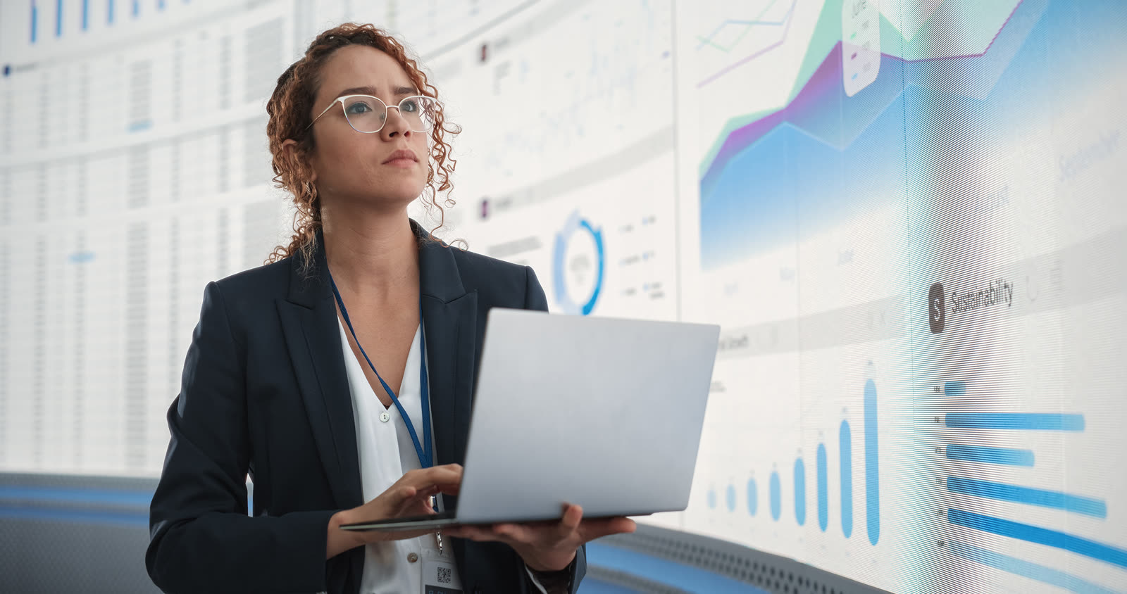 Analyst in glasses looking at large data dashboards