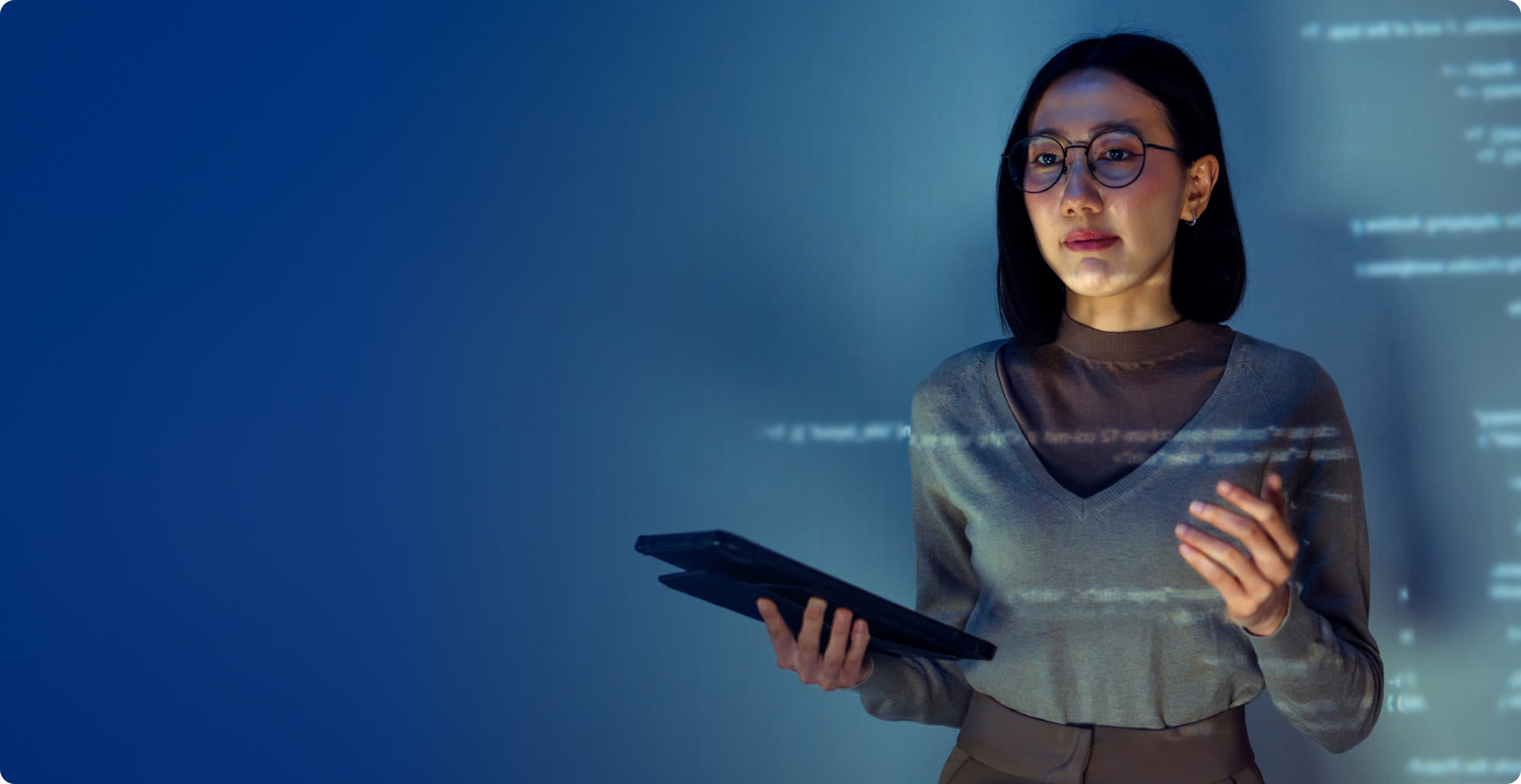 Partner program lead in glasses holding a tablet in front of a wall of projected code