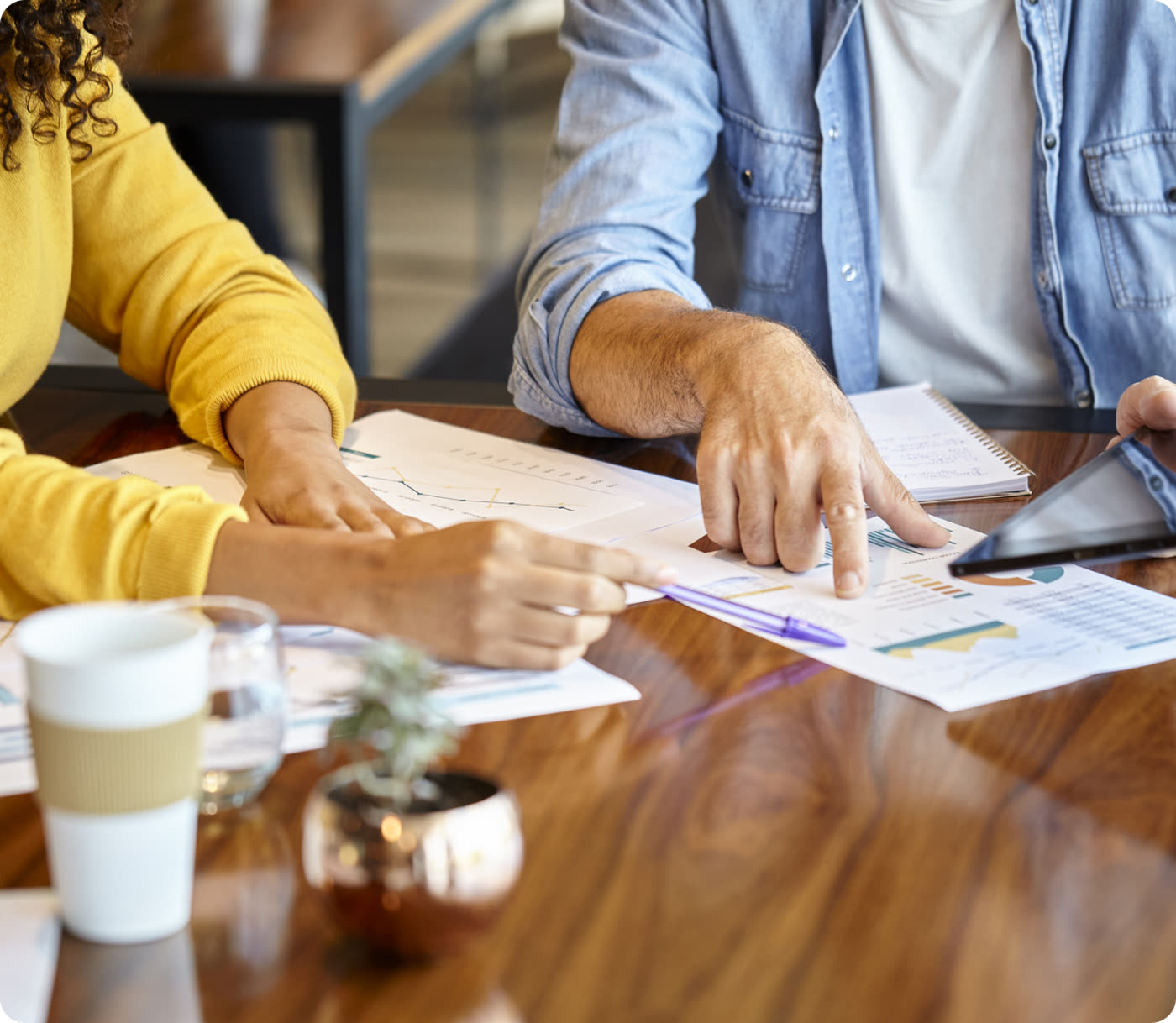 Two colleagues pointing at printed charts and reports across a wooden table
