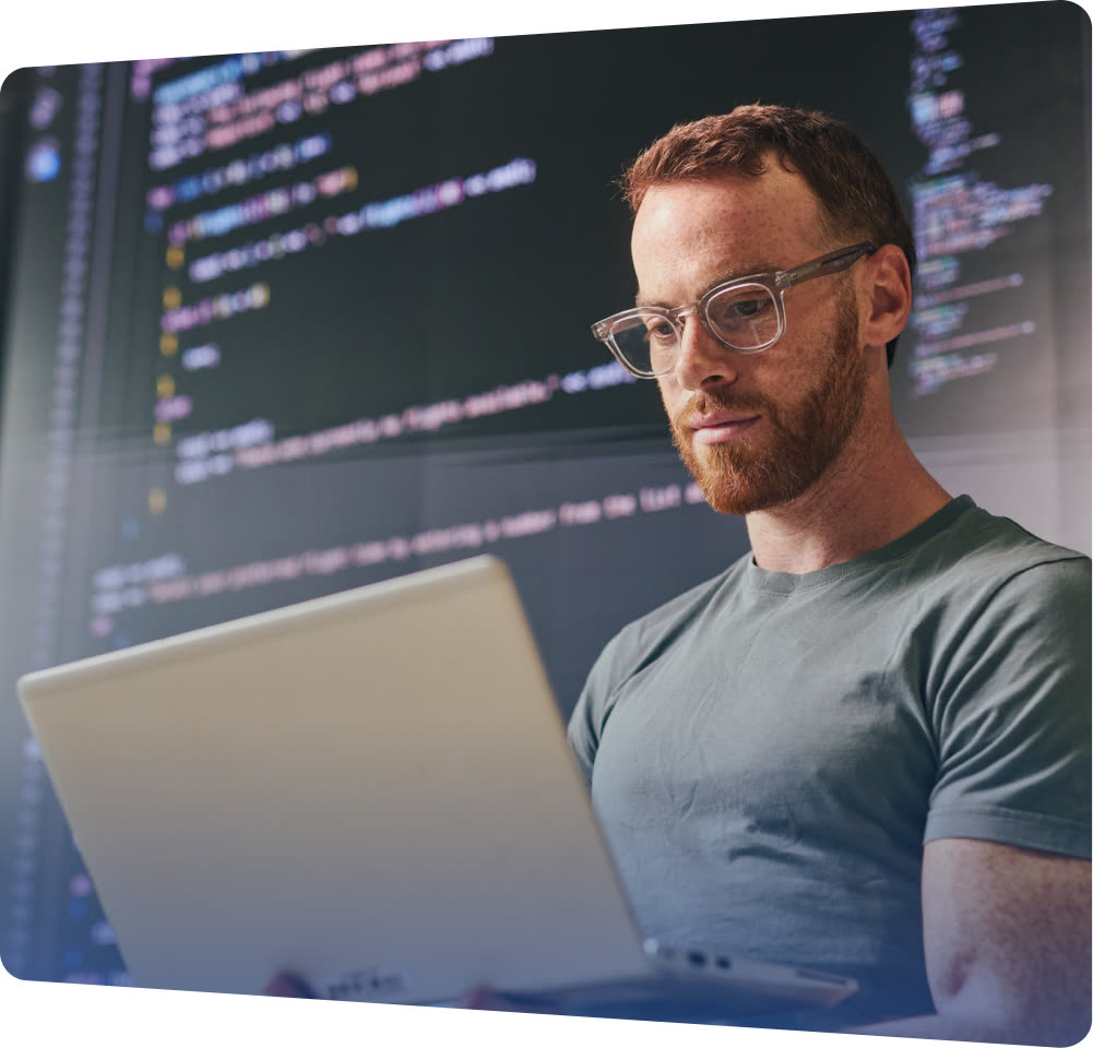 Learner working at a laptop in front of a wall of code